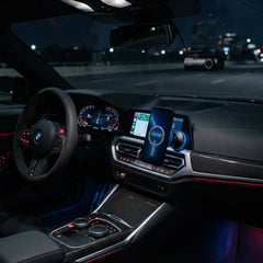 Modern car interior display featuring a windshield-mounted smart dashcam, a smartphone on a magnetic MagSafe air vent mount, and carbon fiber dashboard trim with ambient lighting at night.