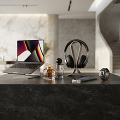 Luxury lifestyle collection display featuring a laptop on a metallic stand, two elegant perfume bottles, premium over-ear headphones on a curved stand, a smartphone, and a smartwatch on a textured dark counter.